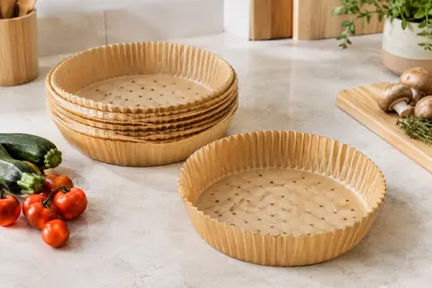 Barquettes rondes beiges en papier de cuisson perforé, empilées sur un plan de travail clair