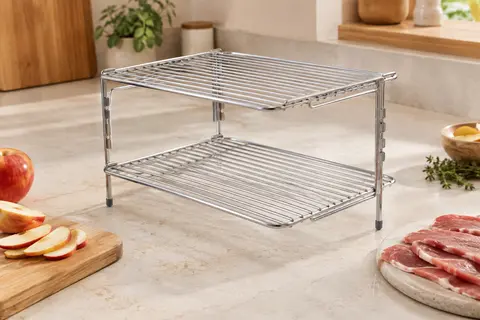 Grille argentée à deux niveaux en acier inoxydable posée sur un plan de travail clair près d’une friteuse à air.