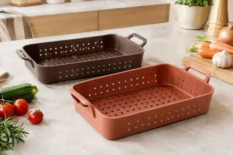 Deux moules en silicone perforés avec poignées, posés sur un plan de travail clair avec des légumes