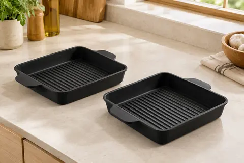 Deux moules carrés noirs en silicone avec fond rainuré et poignées, posés sur un plan de cuisine clair.