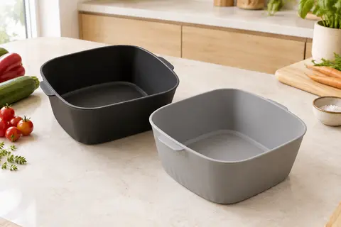 Deux moules carrés en silicone noir et gris pour friteuse à air, posés sur un plan de travail clair.